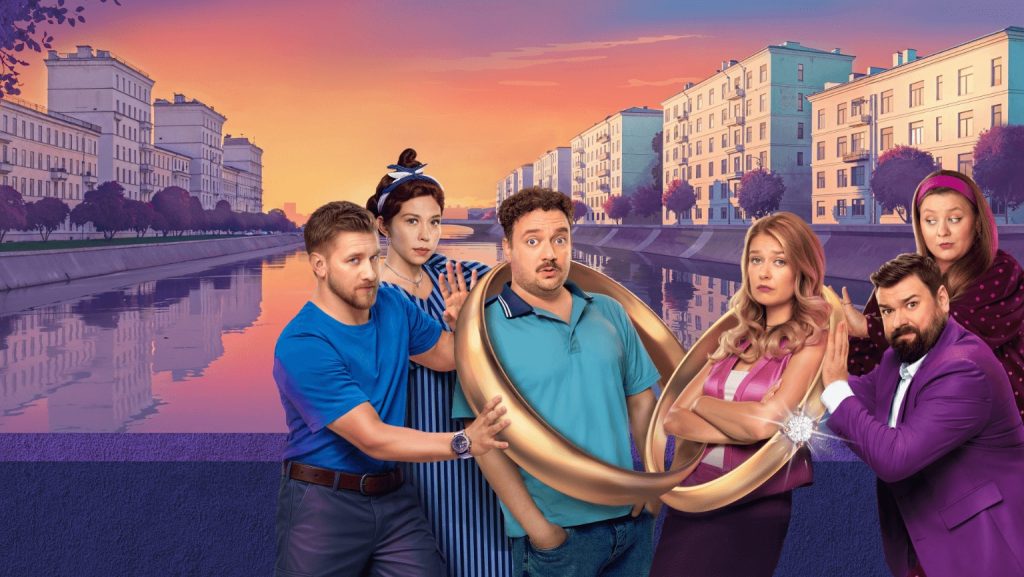 A group of six people entangled in giant gold rings near a river at sunset, symbolizing comedic relationships in the series 'Остаться друзьями.'